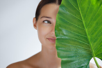 Woman With Perfect Nude Make-up Glowing Skin and a Radiant Smile Behind Big Leaf