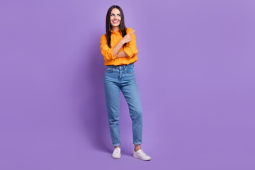 Full body photo of smile girl jeans wear orange shirt direct finger look empty space commercial project isolated on violet color background