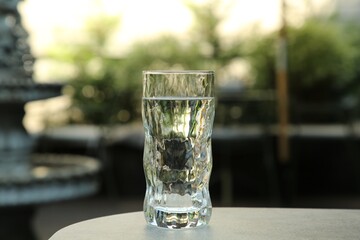 Glass of fresh water on light grey table outdoors