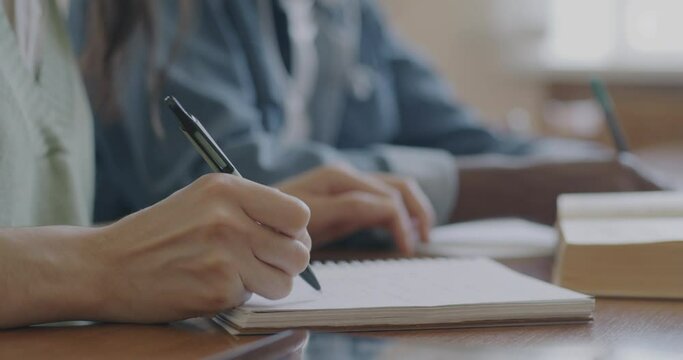 Close-up of hands male and female writing in notebook and touching book at desk in university classroom. Education and people concept.