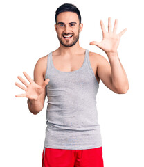 Young handsome man wearing swimwear and sleeveless t-shirt showing and pointing up with fingers number ten while smiling confident and happy.