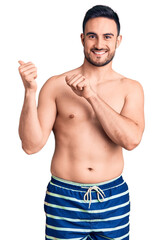 Fototapeta premium Young handsome man wearing swimwear pointing to the back behind with hand and thumbs up, smiling confident