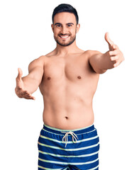 Fototapeta premium Young handsome man wearing swimwear looking at the camera smiling with open arms for hug. cheerful expression embracing happiness.