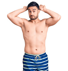 Fototapeta premium Young handsome man wearing swimwear doing bunny ears gesture with hands palms looking cynical and skeptical. easter rabbit concept.