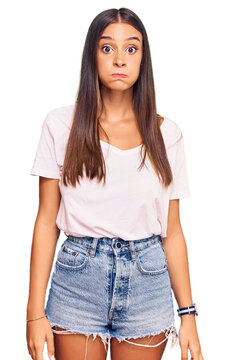 Young hispanic woman wearing casual white tshirt puffing cheeks with funny face. mouth inflated with air, crazy expression.