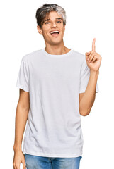 Young hispanic man wearing casual white tshirt pointing finger up with successful idea. exited and happy. number one.