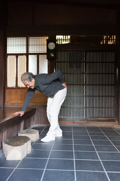 玄関で腰を押さえるシニア男性