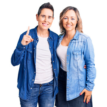 Couple of women wearing casual clothes showing and pointing up with finger number one while smiling confident and happy.