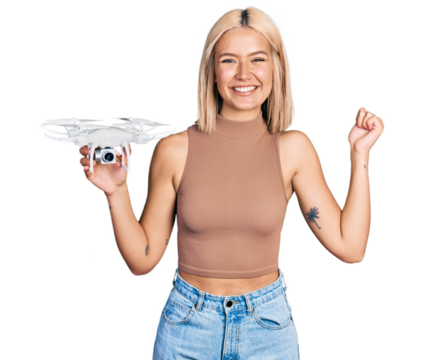 Beautiful young blonde woman holding drone screaming proud, celebrating victory and success very excited with raised arm