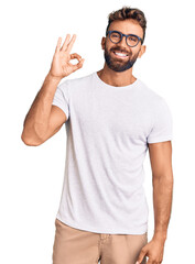 Young hispanic man wearing casual clothes and glasses smiling positive doing ok sign with hand and fingers. successful expression.