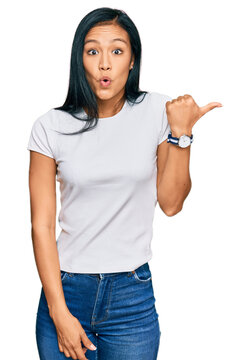 Beautiful hispanic woman wearing casual white tshirt surprised pointing with hand finger to the side, open mouth amazed expression.