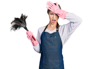 Beautiful young blonde woman wearing apron holding cleaning duster surprised with hand on head for mistake, remember error. forgot, bad memory concept.