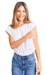 Fototapeta premium Beautiful caucasian woman with blonde hair wearing casual white tshirt cheerful with a smile of face pointing with hand and finger up to the side with happy and natural expression on face