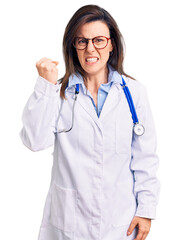 Young beautiful woman wearing doctor stethoscope and glasses angry and mad raising fist frustrated and furious while shouting with anger. rage and aggressive concept.