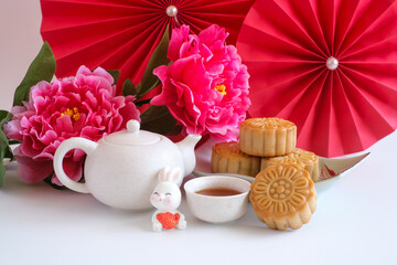 Chinese Mid-Autumn Festival concept made from mooncakes, tea decorated with plum blossom, red paper fans and rabbits isolated on white background.