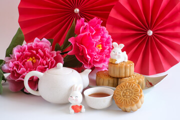 Chinese Mid-Autumn Festival concept made from mooncakes, tea decorated with plum blossom, red paper fans and rabbits isolated on white background.