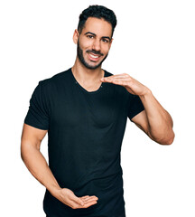 Hispanic man with beard wearing casual black t shirt gesturing with hands showing big and large size sign, measure symbol. smiling looking at the camera. measuring concept.