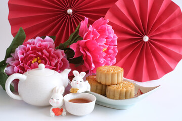 Chinese Mid-Autumn Festival concept made from mooncakes, tea decorated with plum blossom, red paper fans and rabbits isolated on white background.