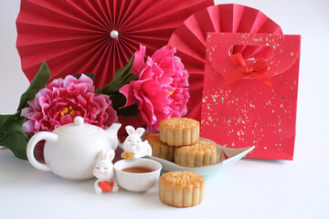 Chinese Mid-Autumn Festival concept made from mooncakes, tea decorated with plum blossom, red paper fans, red bag and rabbits isolated on white background.