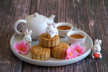 Chinese Mid-Autumn Festival concept made from mooncakes, tea decorated with plum blossom and rabbits on wooden background.