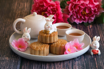 Chinese Mid-Autumn Festival concept made from mooncakes, tea decorated with plum blossom and rabbits on wooden background.