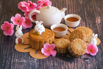 Chinese Mid-Autumn Festival concept made from mooncakes, tea decorated with plum blossom and rabbits on wooden background.