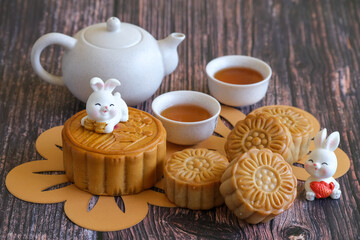Chinese Mid-Autumn Festival concept made from mooncakes, tea decorated with plum blossom and rabbits on wooden background.