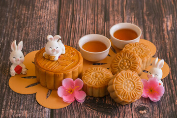 Chinese Mid-Autumn Festival concept made from mooncakes, tea decorated with plum blossom and rabbits on wooden background.