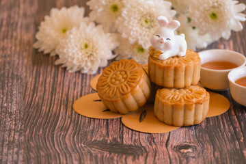 Obraz na płótnie Canvas Chinese Mid-Autumn Festival concept made from mooncakes, tea decorated with Chrysanthemum blossom and rabbit on wooden background.