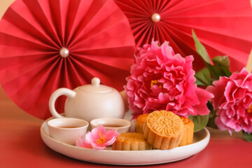 Chinese Mid-Autumn Festival concept made from mooncakes, tea decorated with plum blossom, rabbit and red paper fans on red background.