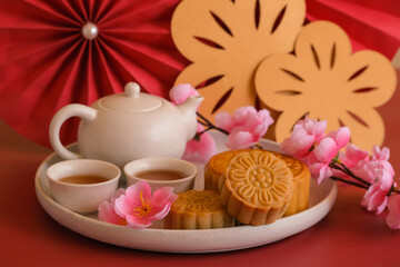 Chinese Mid-Autumn Festival concept made from mooncakes, tea decorated with plum blossom, rabbit and red paper fans on red background.