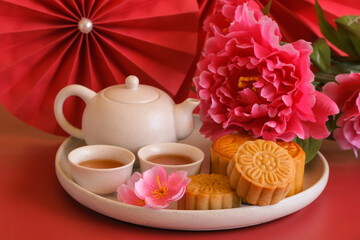 Chinese Mid-Autumn Festival concept made from mooncakes, tea decorated with plum blossom, rabbit and red paper fans on red background.