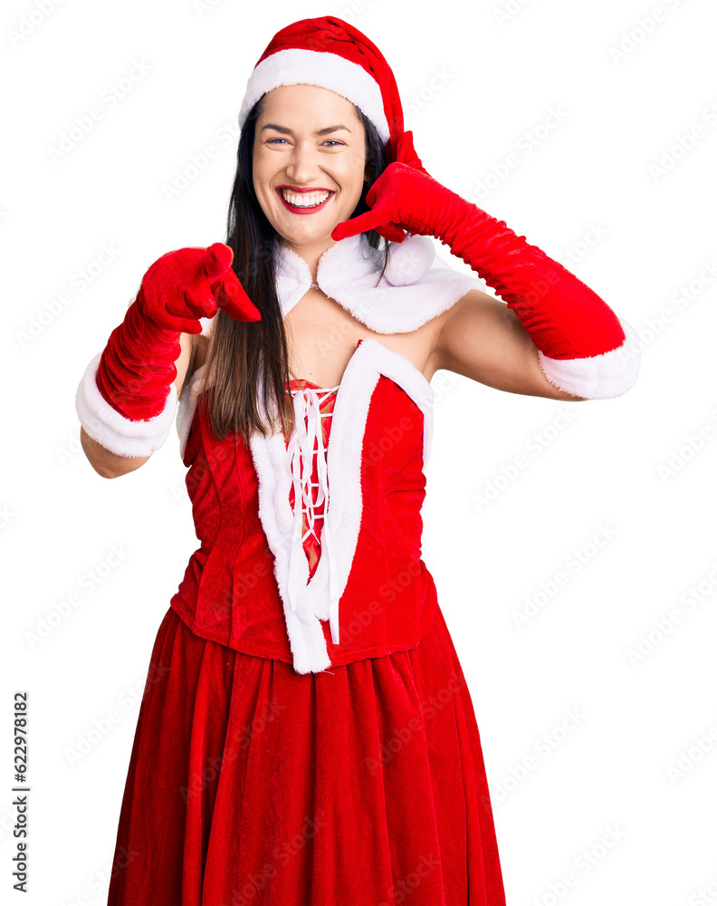 Sticker Young beautiful caucasian woman wearing santa claus costume smiling doing talking on the telephone gesture and pointing to you. call me.