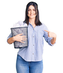 Young beautiful girl holding paper bin full of crumpled papers pointing finger to one self smiling happy and proud