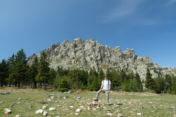 The guy, a tourist, stands tall against the background of a rock. Summer, day, blue sky.