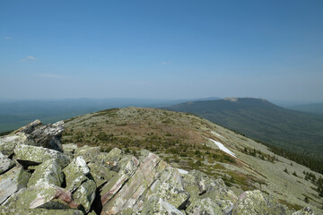 Panorama, landscape. In the foreground are rocks covered with moss, in the background are mountains. Summer, blue sky, day.