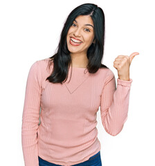 Young hispanic woman wearing casual clothes smiling with happy face looking and pointing to the side with thumb up.