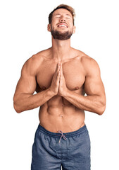 Fototapeta premium Young caucasian man standing shirtless begging and praying with hands together with hope expression on face very emotional and worried. begging.