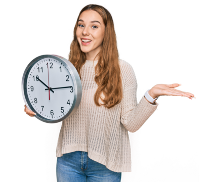 Young blonde woman holding big clock celebrating victory with happy smile and winner expression with raised hands