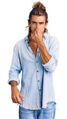 Young hispanic man wearing summer style smelling something stinky and disgusting, intolerable smell, holding breath with fingers on nose. bad smell
