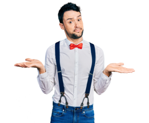 Hispanic man with beard wearing hipster look with bow tie and suspenders clueless and confused expression with arms and hands raised. doubt concept.