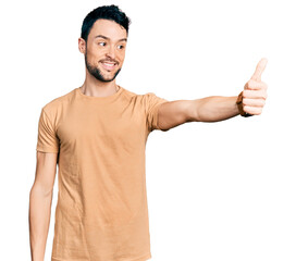 Hispanic man with beard wearing casual t shirt looking proud, smiling doing thumbs up gesture to the side
