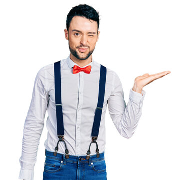 Hispanic man with beard presenting with open palm winking looking at the camera with sexy expression, cheerful and happy face.