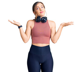 Beautiful caucasian young woman wearing gym clothes and using headphones clueless and confused...