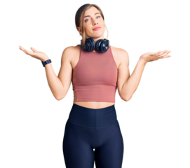 Beautiful caucasian young woman wearing gym clothes and using headphones clueless and confused expression with arms and hands raised. doubt concept.