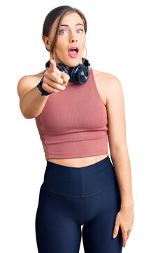 Beautiful caucasian young woman wearing gym clothes and using headphones pointing displeased and frustrated to the camera, angry and furious with you