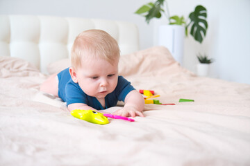 baby boy in blue bodysuit playing with colorful plastic toys on bed
