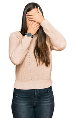 Young brunette woman wearing casual winter sweater covering eyes and mouth with hands, surprised and shocked. hiding emotion