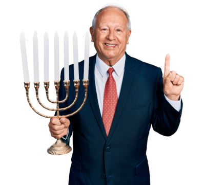 Senior business man with grey hair holding menorah hanukkah jewish candle smiling with an idea or question pointing finger with happy face, number one