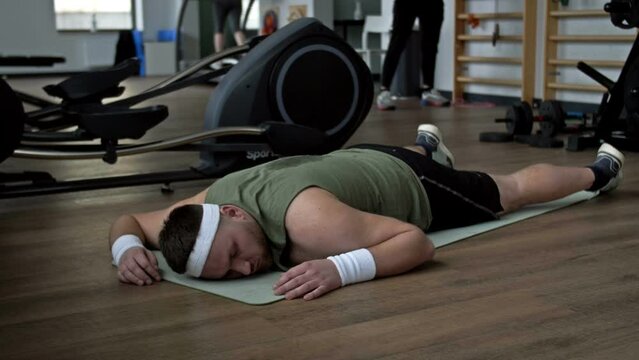 Tired from physical activity, a young overweight man lies prone on a karemat in the gym.